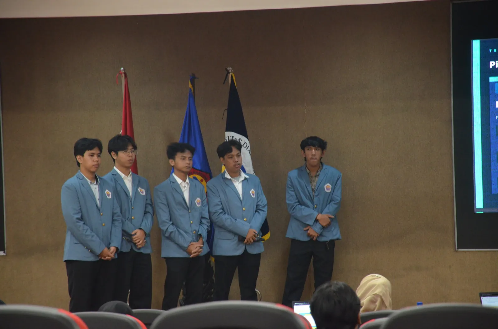 Tim berjas almamater biru berdiri di depan layar presentasi pada acara final ICBC 2026